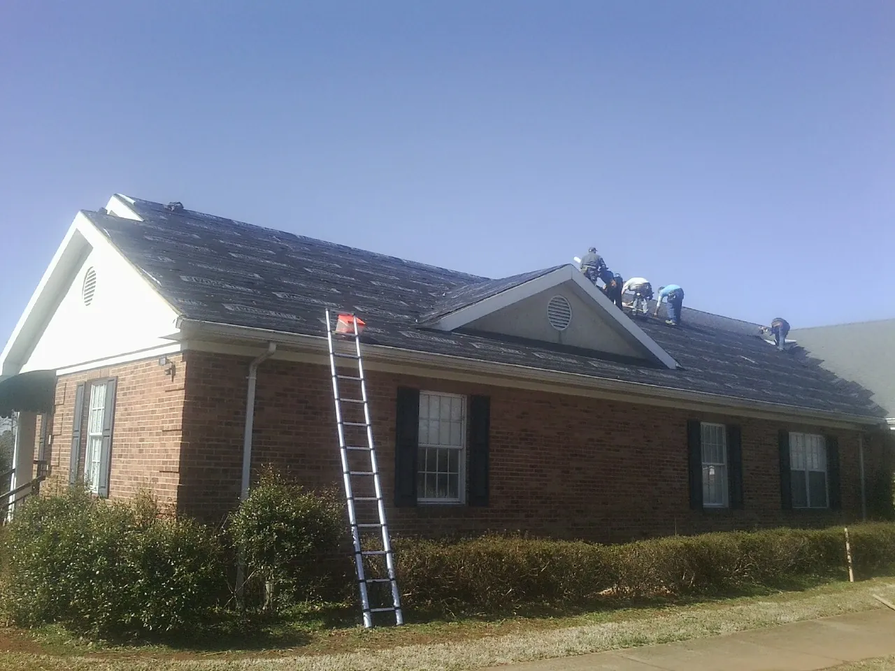 Crew tearing shingles off a brick ranch roof with a ladder set — Metal Roof Repair work by our crew in Armagh