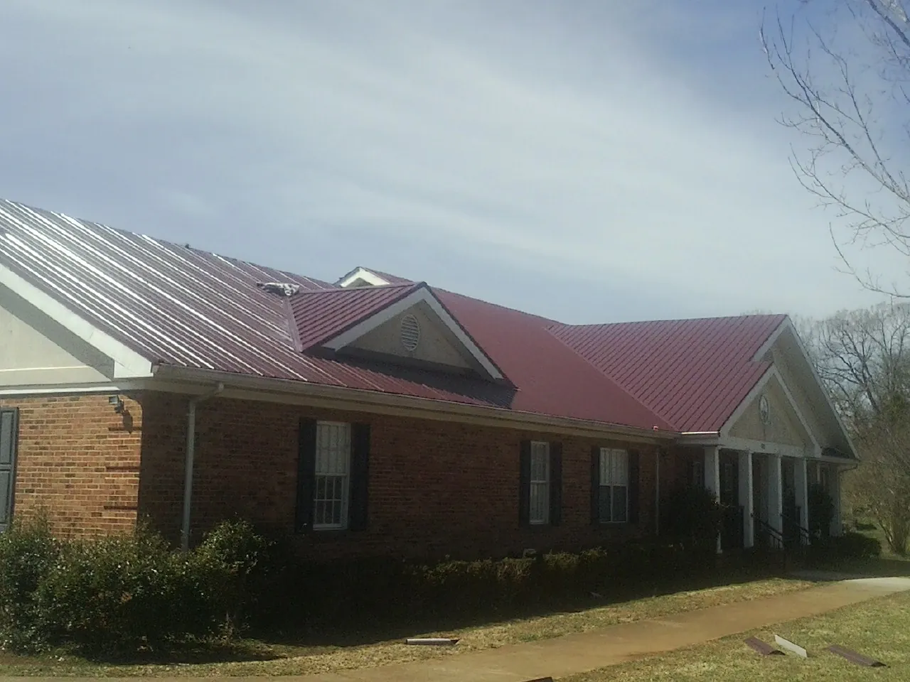 Red metal roof with gabled entries on a long brick building, from a Hail Damage Roof Repair job in Armagh