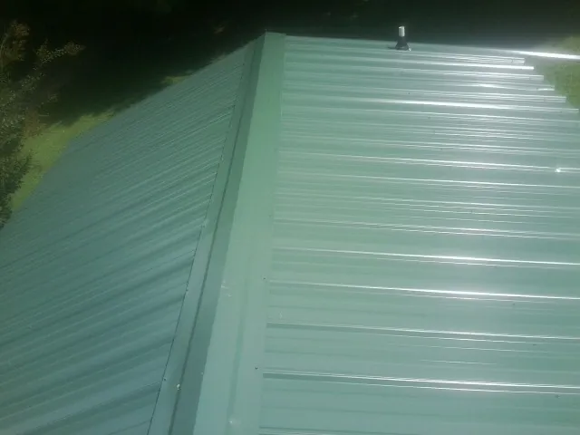 New green metal panels meeting at the ridge of a roof — Flat Roof Repair work by our crew in Armagh