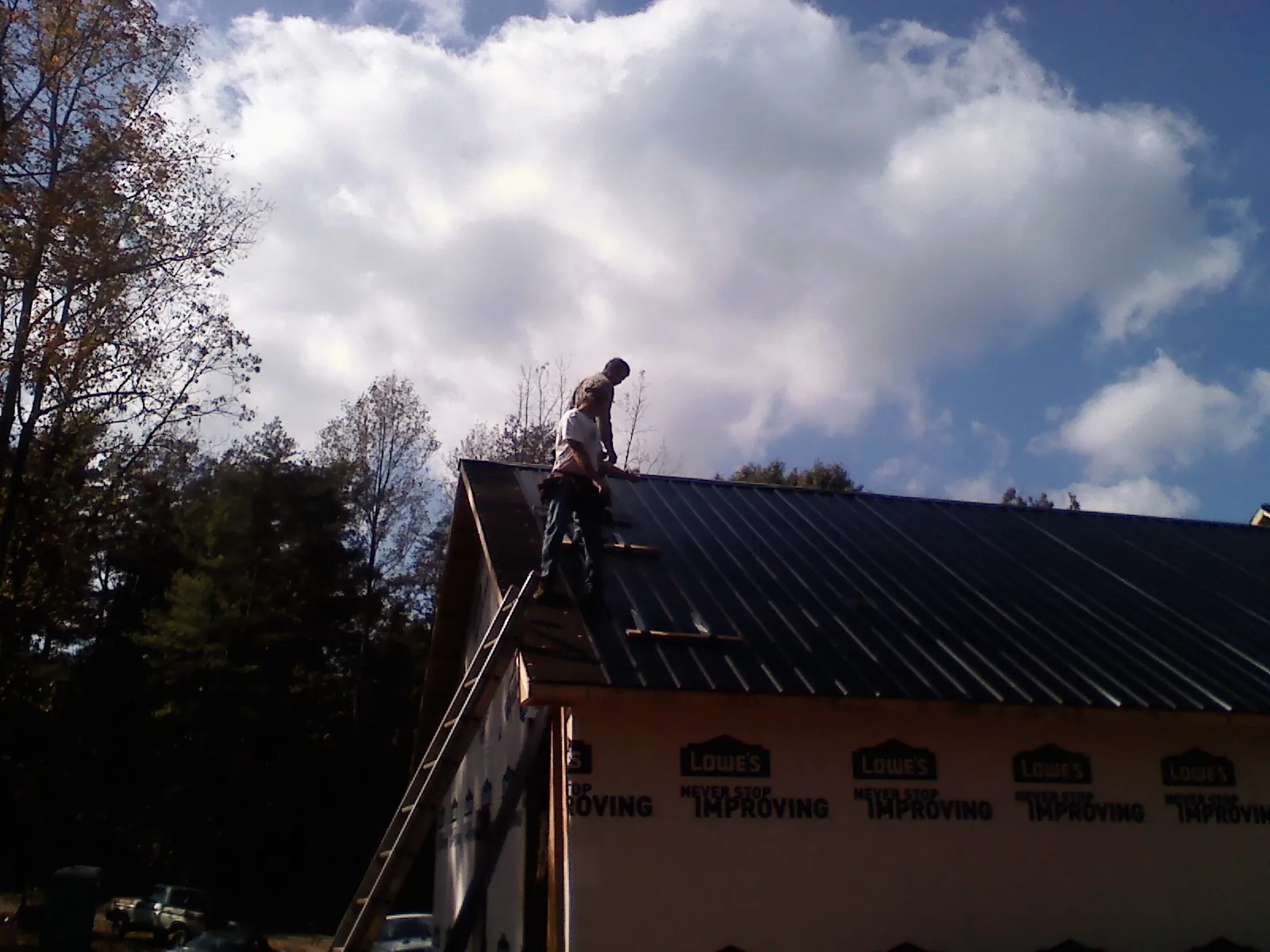 Roofer fastening dark metal panels high against a cloudy sky, from a Roof Inspection job in Armagh