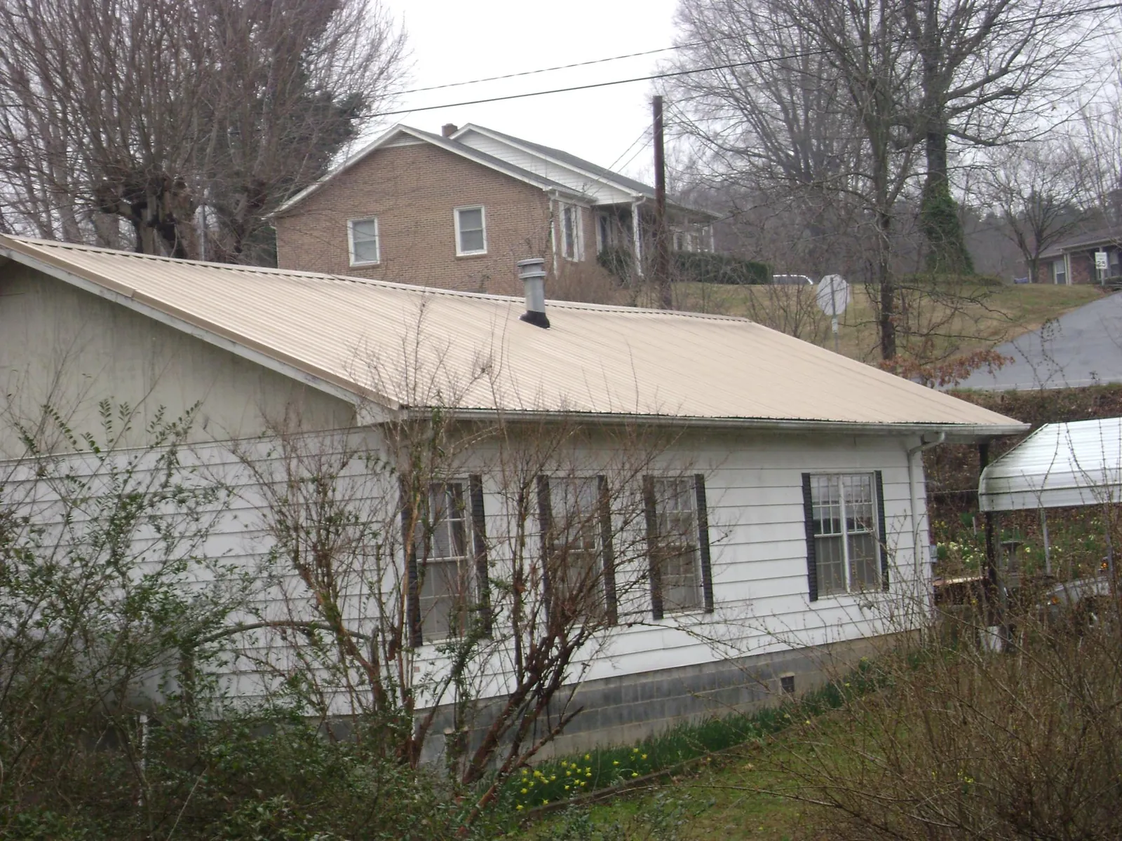 Tan metal roof on a white sided house set into a hillside — Commercial Roofing by Roofing Brothers in Armagh